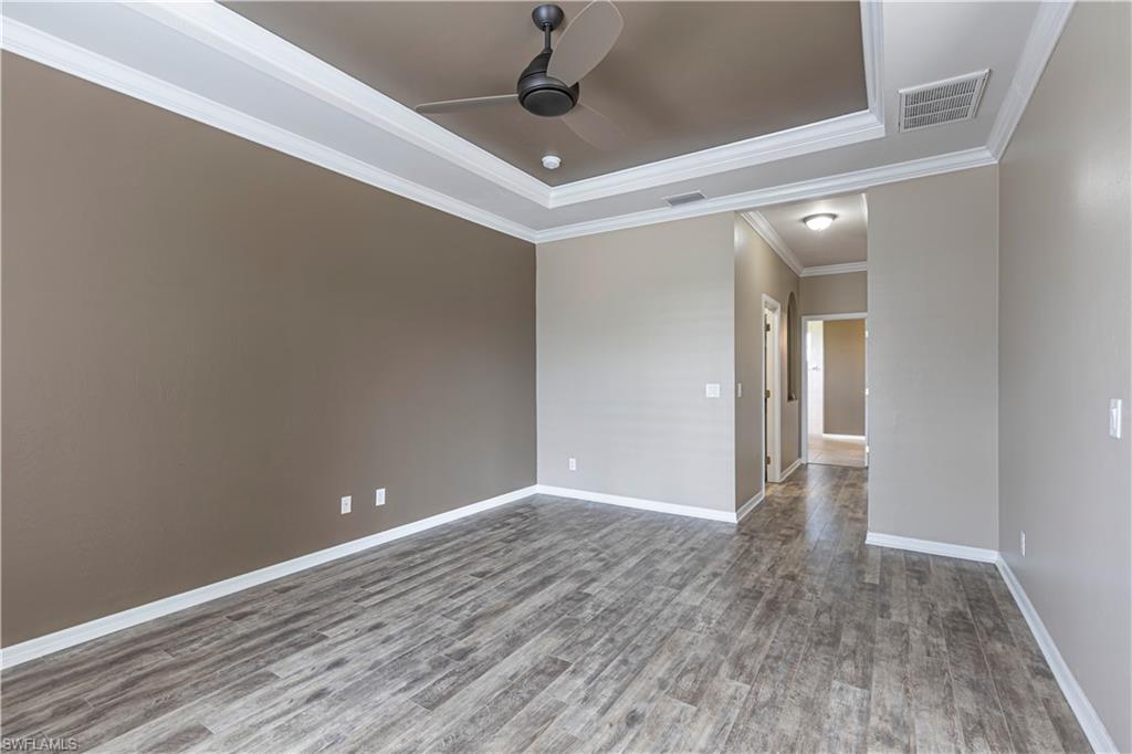 Spacious room featuring wood-finish flooring, a tray ceiling with crown molding, and a ceiling fan