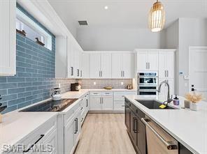 Kitchen featuring white cabinetry, light wood-finish flooring, a large island with sink, integrated double ovens, and a striking blue subway tile accent wall with a transom window