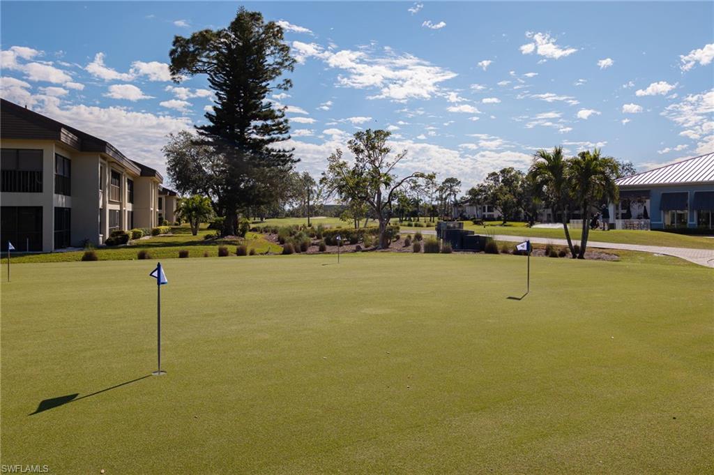 Manicured putting green with multiple flagsticks, bordered by mature trees and residential buildings