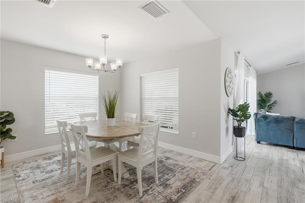 Open-concept dining area featuring light wood-finish flooring, two large windows with horizontal blinds, and a contemporary five-light chandelier