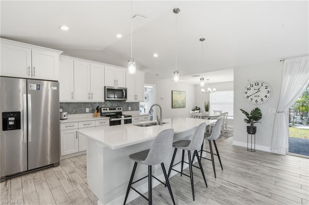 Modern kitchen featuring a large center island with pendant lighting, stainless steel appliances, and white cabinetry