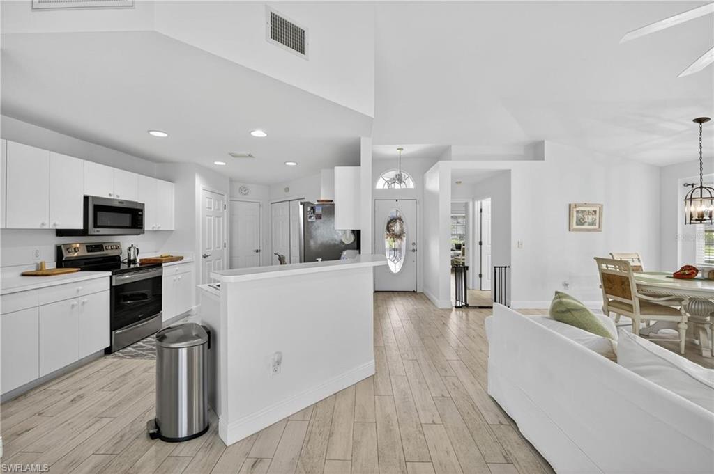 Open-concept kitchen and living area featuring wood-finish flooring, white cabinetry, recessed lighting, and stainless steel appliances