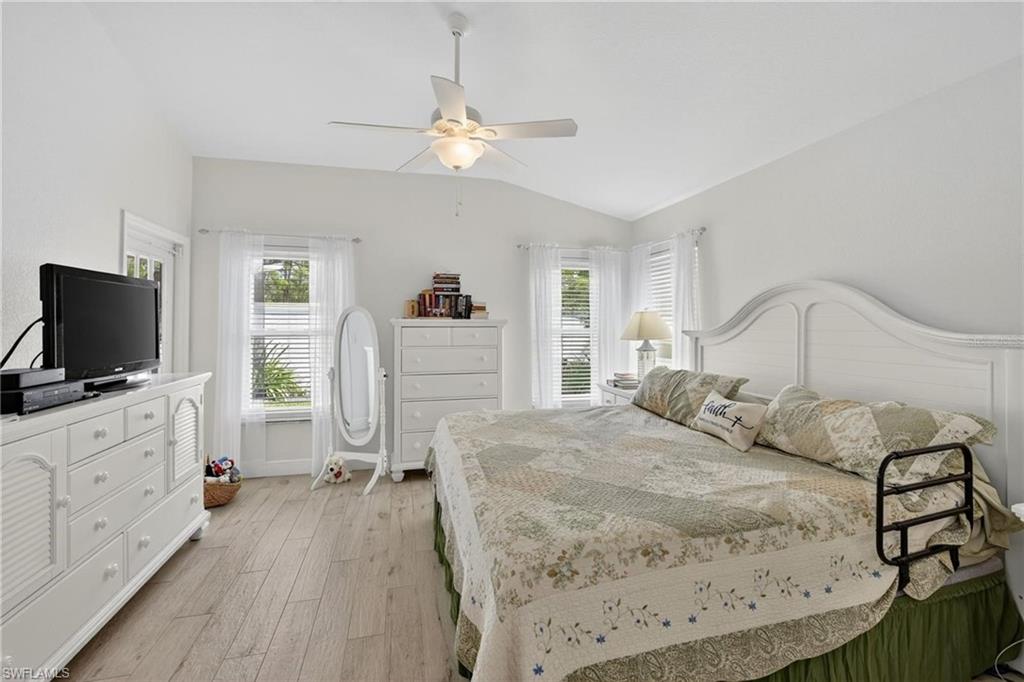 Spacious room featuring vaulted ceilings, light wood-finish flooring, multiple windows with blinds, and a ceiling fan with integrated lighting