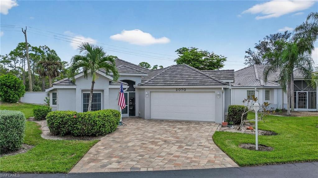 Contemporary stucco exterior with a tiled roof, featuring a paver driveway, an attached garage, and manicured landscaping