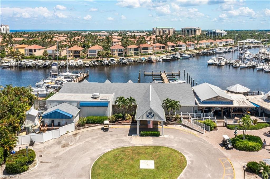 Marina complex featuring multiple boat slips, a central club building with a covered entrance, a waterfront dining establishment with outdoor seating, and surrounding residential properties with water access