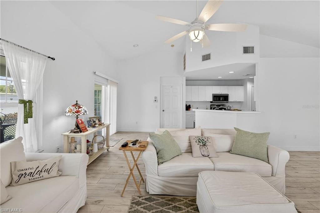 Open-concept living area with vaulted ceilings, wood-finish flooring, a ceiling fan, and sliding glass doors to the exterior