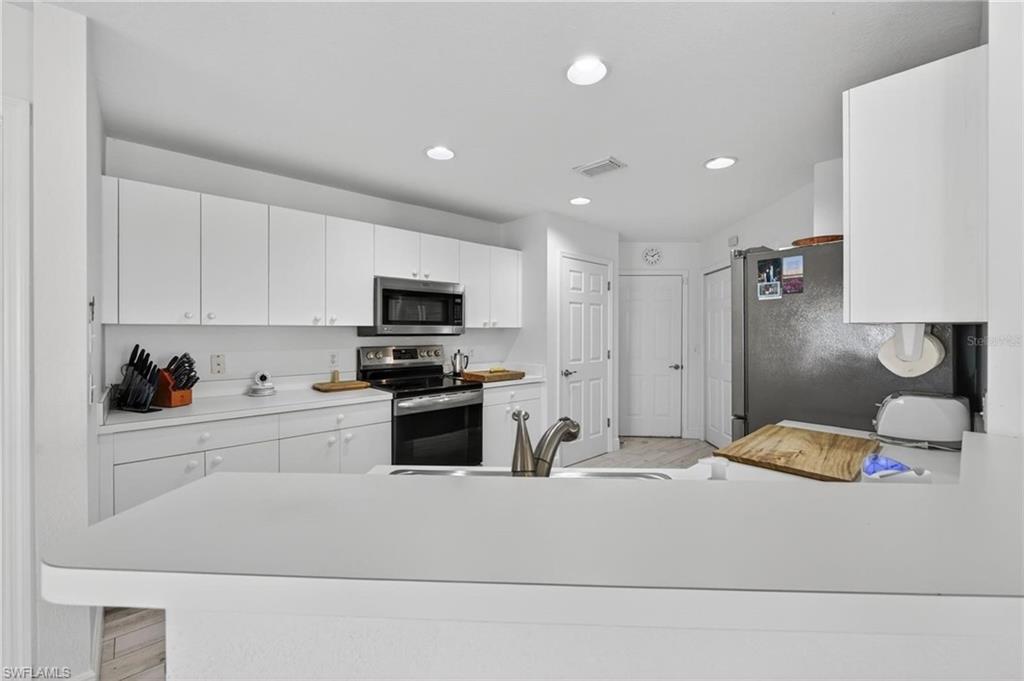 Kitchen featuring white cabinetry, light-toned countertops, stainless steel appliances, a kitchen island with an integrated sink, and recessed lighting