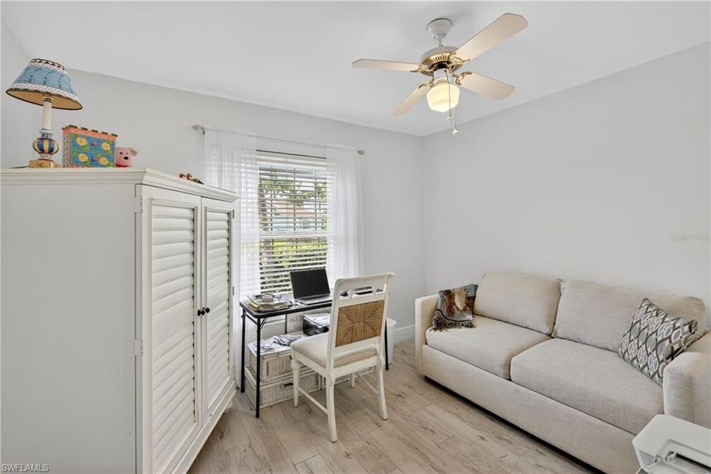 Light-filled room featuring wood-finish flooring, a ceiling fan with integrated lighting, and a window dressed with white blinds and sheer curtains