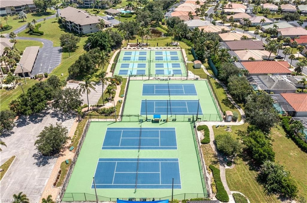 Six tennis courts with blue playing surfaces and light green surrounds, bordered by landscaping and paved pathways