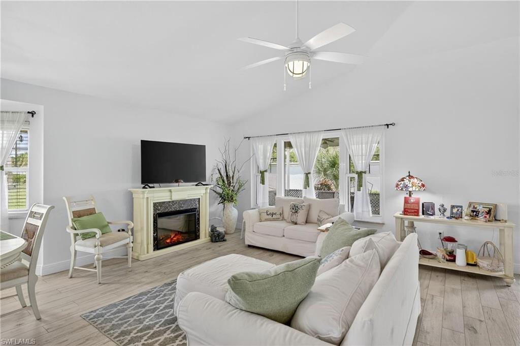 Spacious living area featuring light wood-finish flooring, an electric fireplace with a decorative mantel, and a vaulted ceiling with a ceiling fan