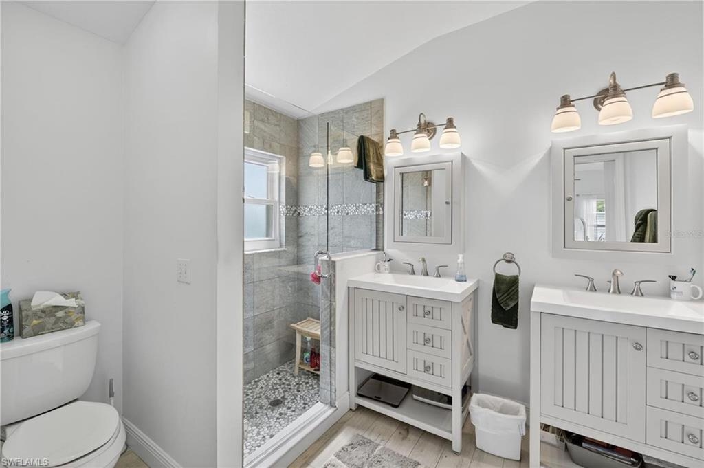 Bathroom featuring a glass-enclosed shower with pebble flooring and a window, dual vanity sinks with white cabinetry, and individual framed mirrors