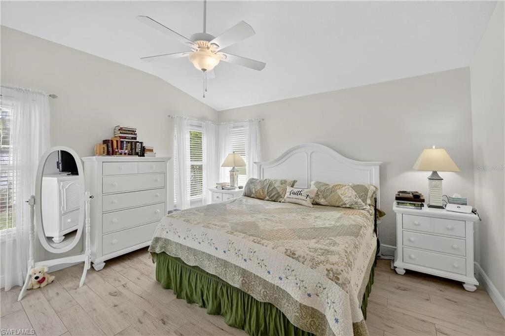 Vaulted ceiling with a ceiling fan, light-toned wood-finish flooring, white walls, and multiple windows with white blinds