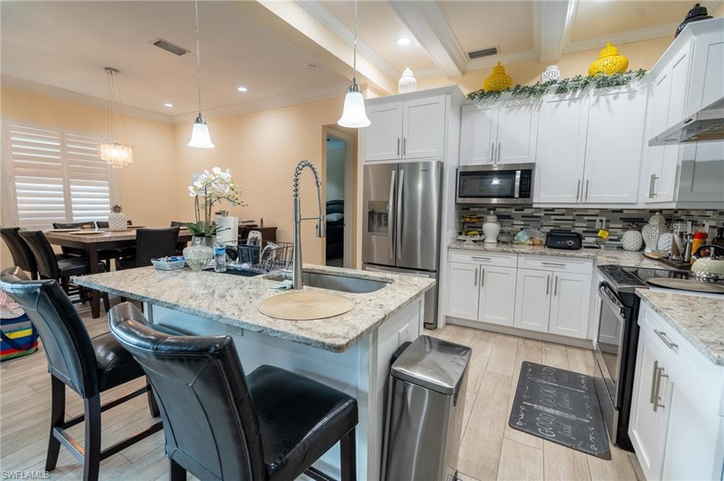 Open-concept kitchen featuring an eat-at island with a stainless steel sink, granite countertops, white cabinetry, and stainless steel appliances