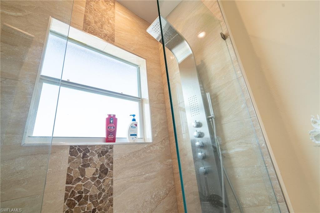 Tiled shower enclosure featuring a multi-function shower panel, a framed window, and a decorative mosaic tile accent