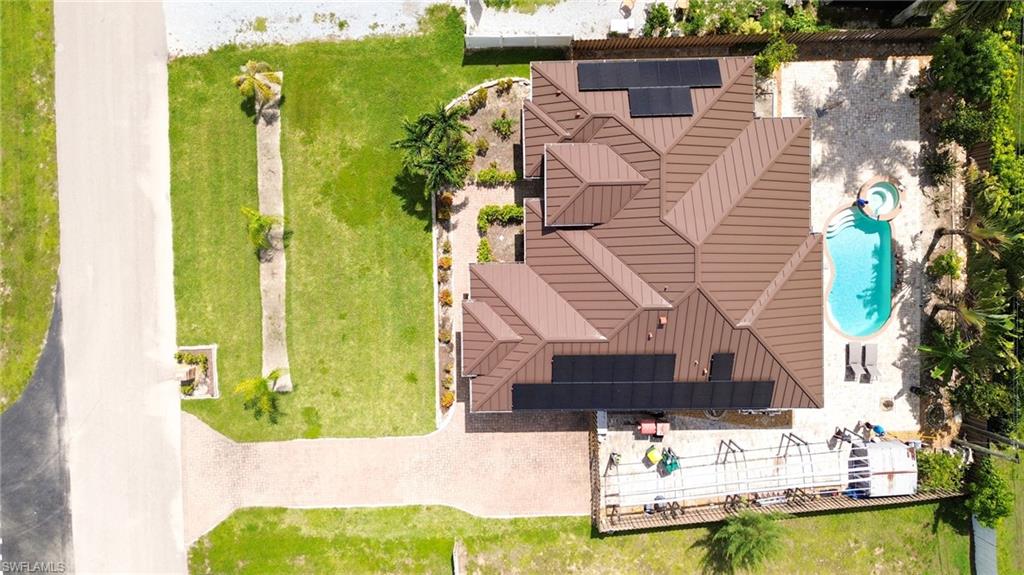 Expansive property featuring a brown metal roof, solar panels, and a free-form swimming pool with surrounding patio
