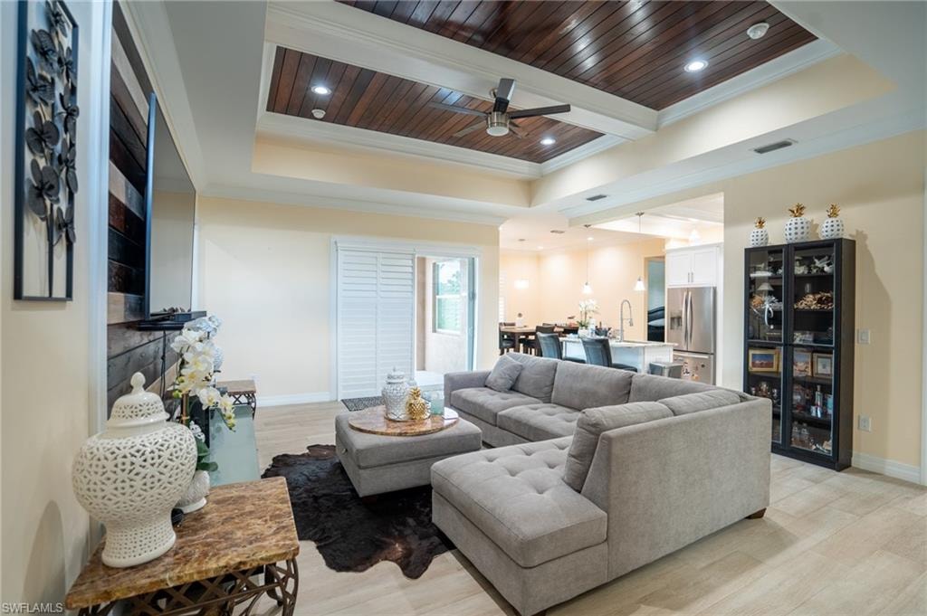 Spacious living area featuring a wood-panel tray ceiling with recessed lighting and a ceiling fan