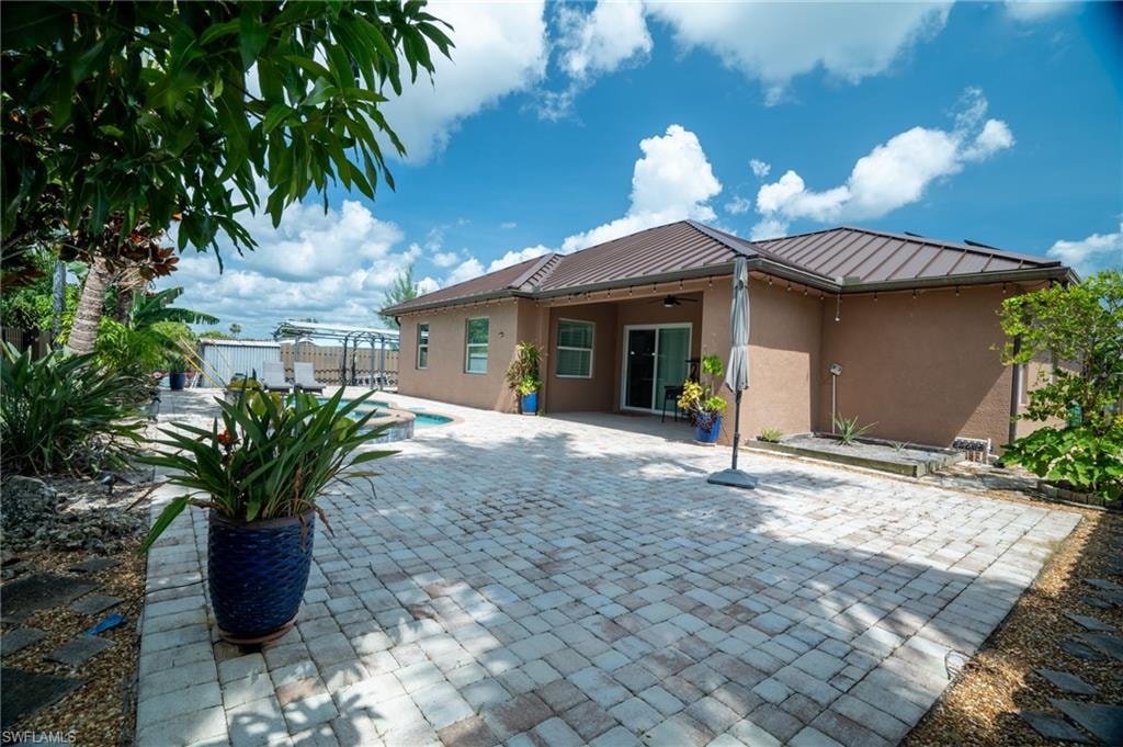Spacious paver patio featuring a built-in pool with spa, stucco exterior, and a brown metal roof