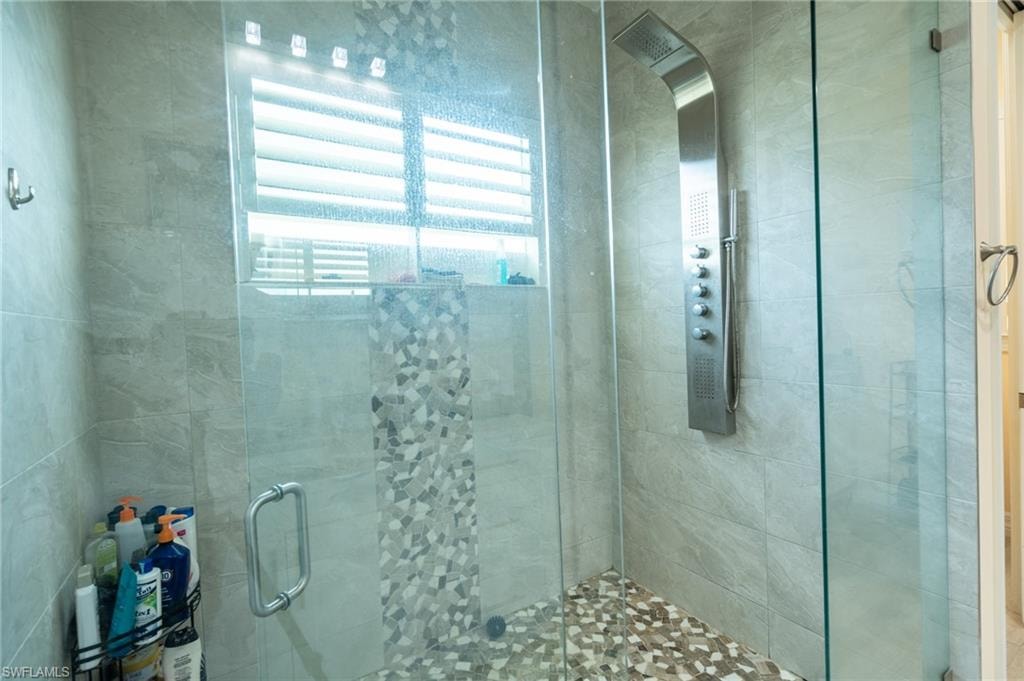 Glass-enclosed shower featuring a multi-function shower panel, stone tile flooring, and a mosaic tile accent strip