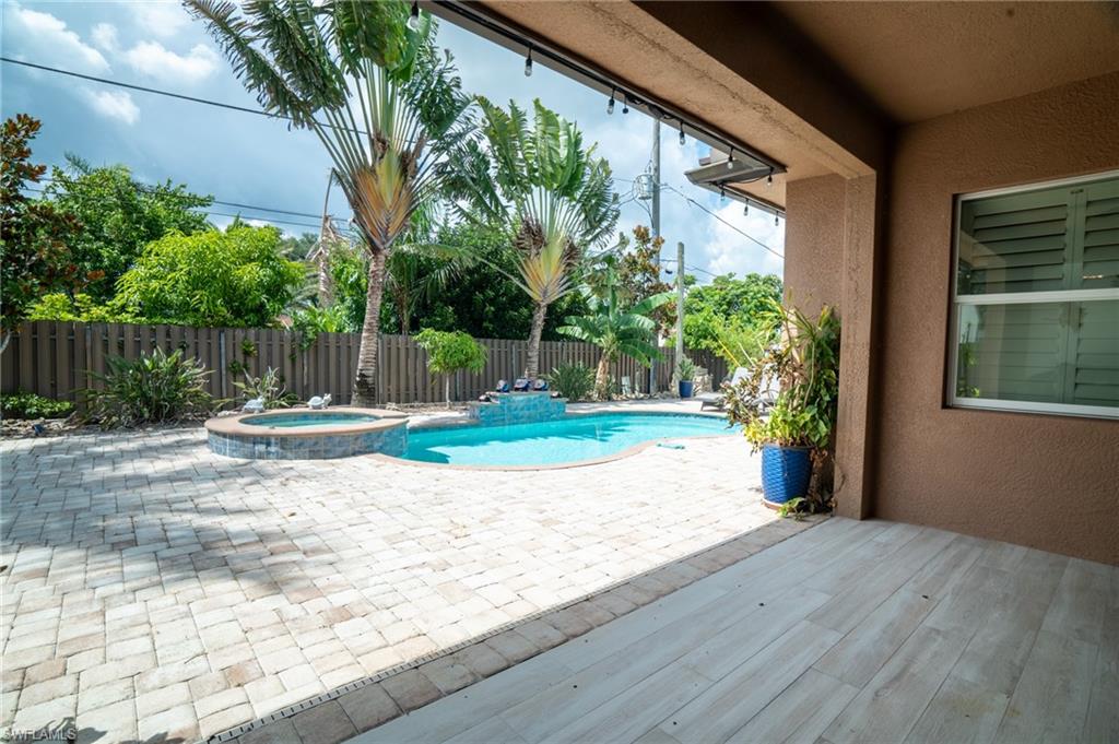 Covered patio featuring wood-finish flooring extending to a paver patio with an in-ground pool and integrated spa