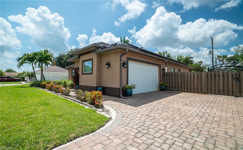Exterior featuring a paver driveway, an attached garage, a manicured lawn, established landscaping, and a privacy fence