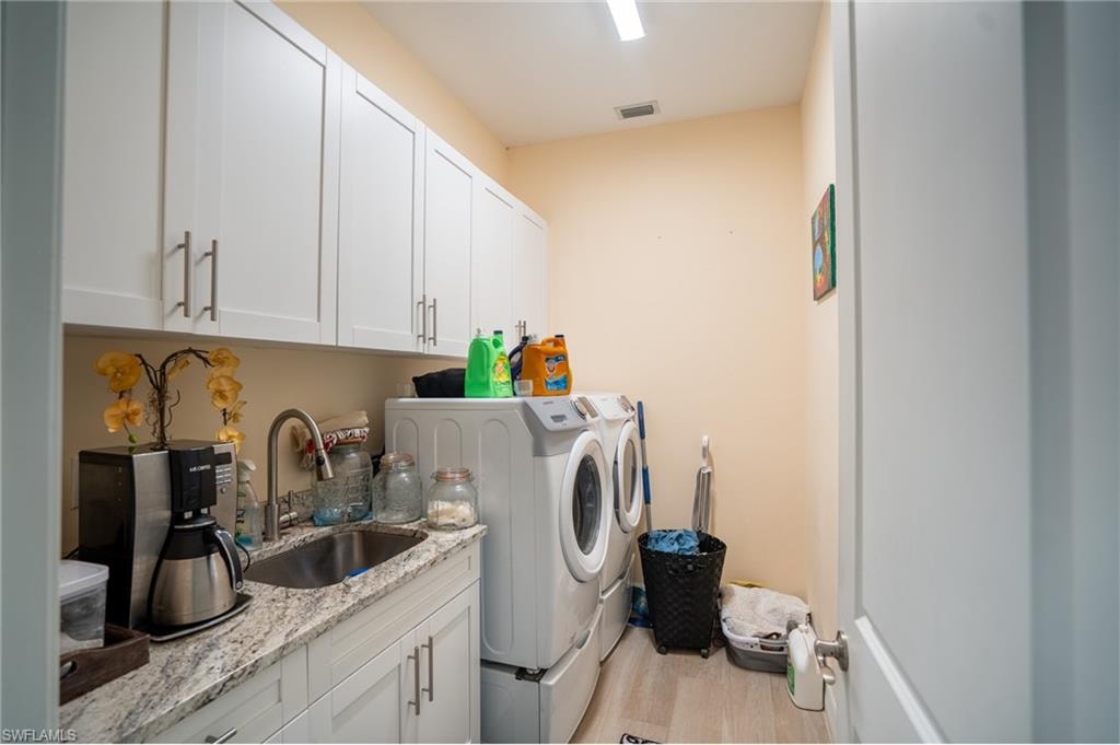 Utility room featuring light wood-finish flooring, white upper and lower cabinetry, a light-toned countertop, and a stainless steel sink with a gooseneck faucet