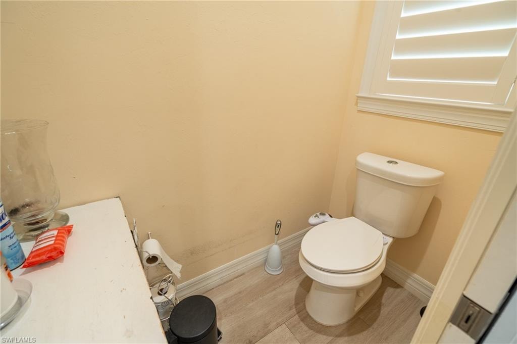Compact powder room featuring a white toilet with an attached bidet, light wood-finish flooring, and a window with white plantation shutters