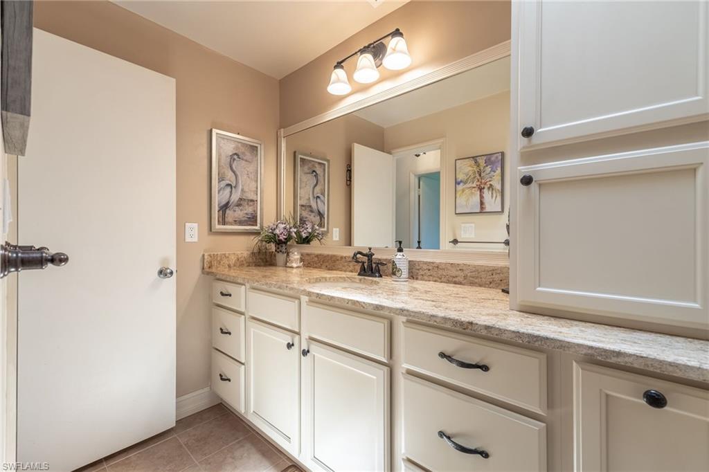 Bathroom vanity featuring extensive counter space with a light-toned, speckled finish, ample white cabinetry and drawers with dark hardware, a single basin sink with a dark faucet, and an expansive wall mirror