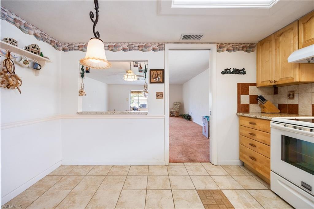 Kitchen featuring wood cabinetry, white appliances, checkered tile backsplash, and a pass-through window with a stone-look countertop