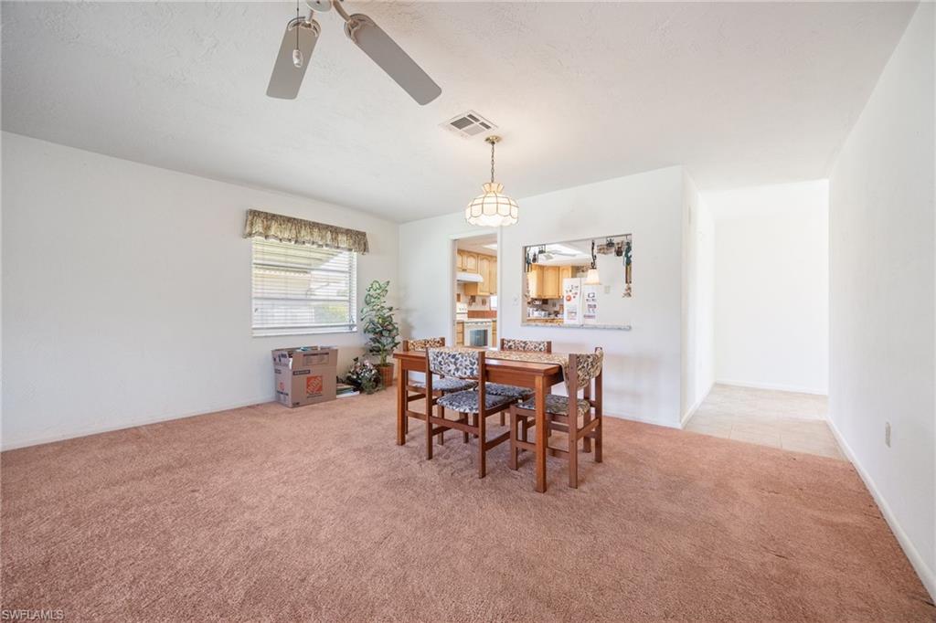 Dining area featuring a pass-through window, carpet flooring, a ceiling fan, and a suspended light fixture