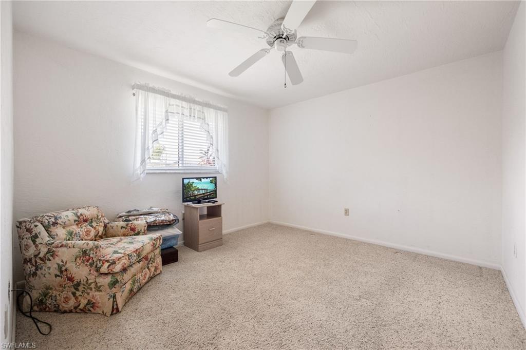 Bright interior space featuring a window with horizontal blinds, a ceiling fan with light fixture, and neutral carpeting