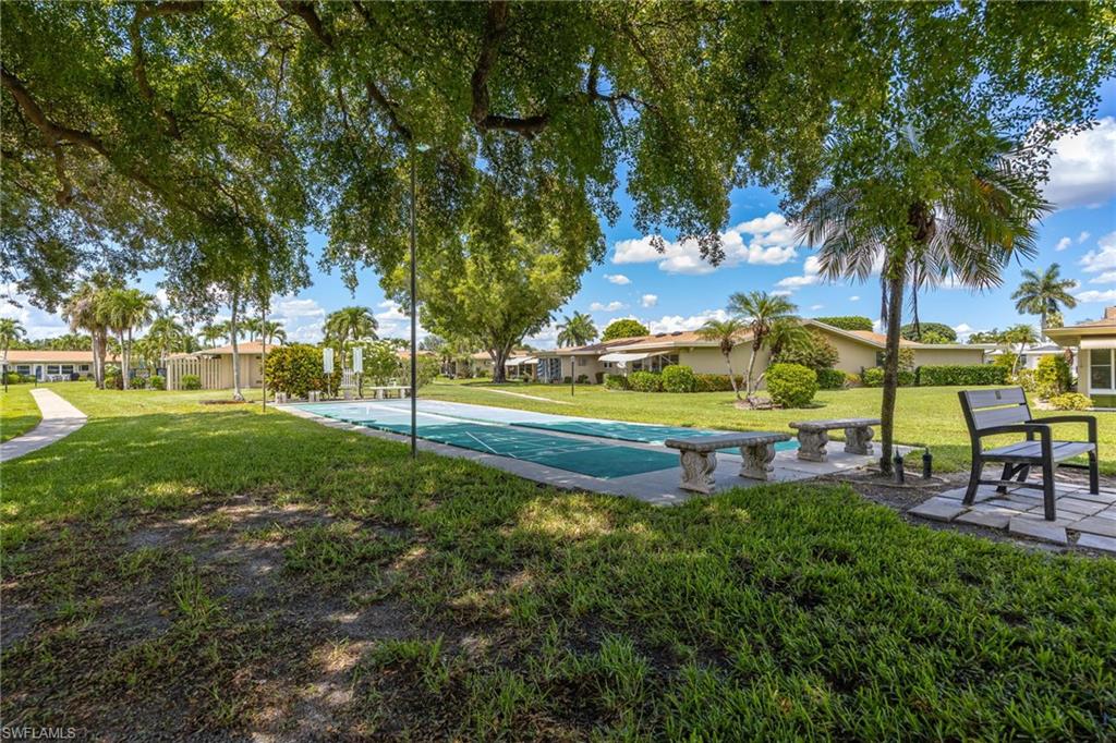 Outdoor shuffleboard court with surrounding green space, mature trees, and landscaping
