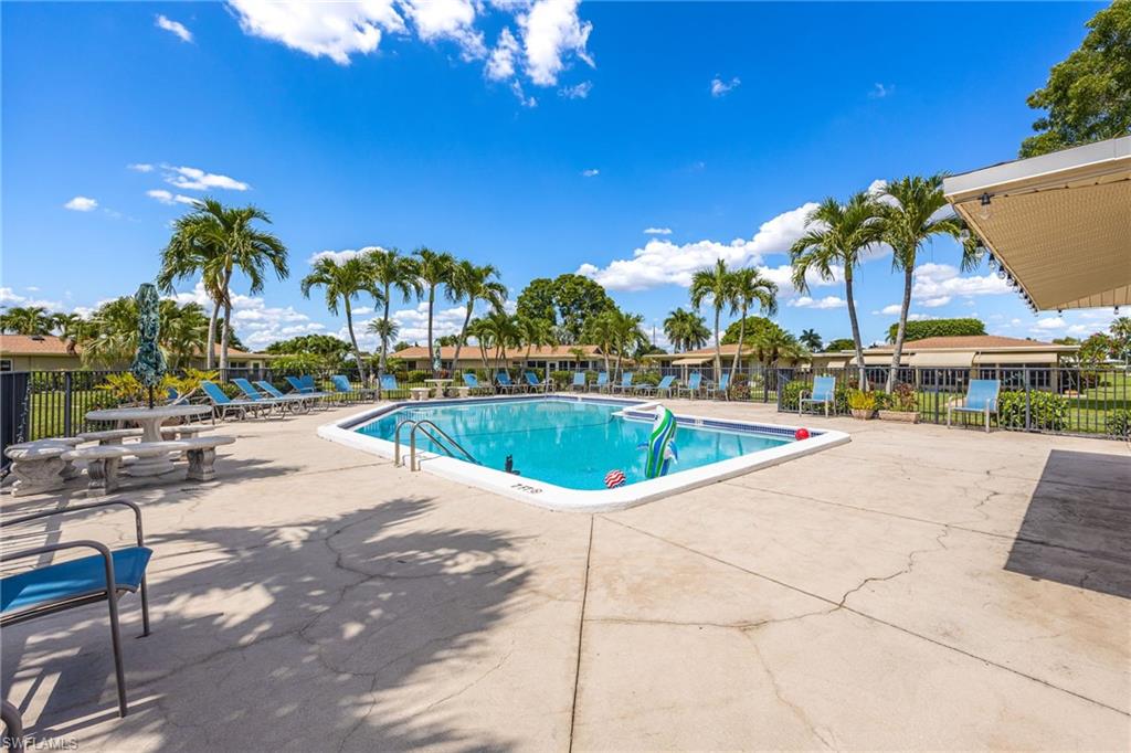 Outdoor swimming pool with concrete decking, surrounded by palm trees and lounge chairs