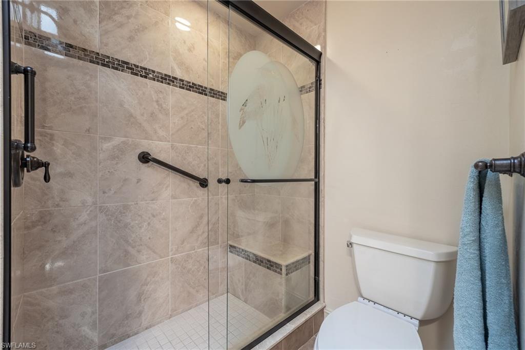 Shower enclosure featuring full-height stone-look tile, a decorative mosaic accent band, and a built-in bench