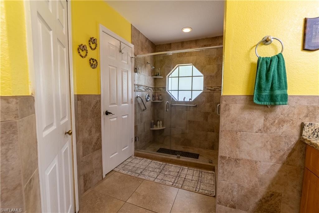 Bathroom with tile walls, vanity, a stall shower, tile patterned flooring, and wainscoting