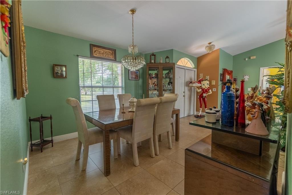 Dining room featuring light tile patterned flooring, baseboards, vaulted ceiling, and an inviting chandelier