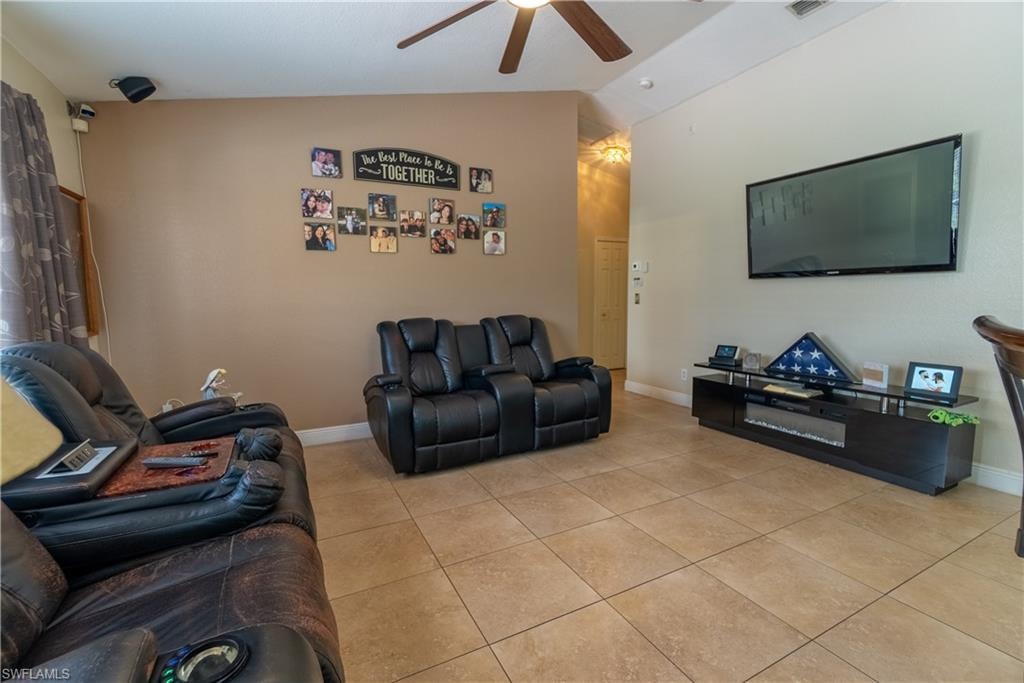 Living area featuring light tile patterned flooring, baseboards, lofted ceiling, and ceiling fan