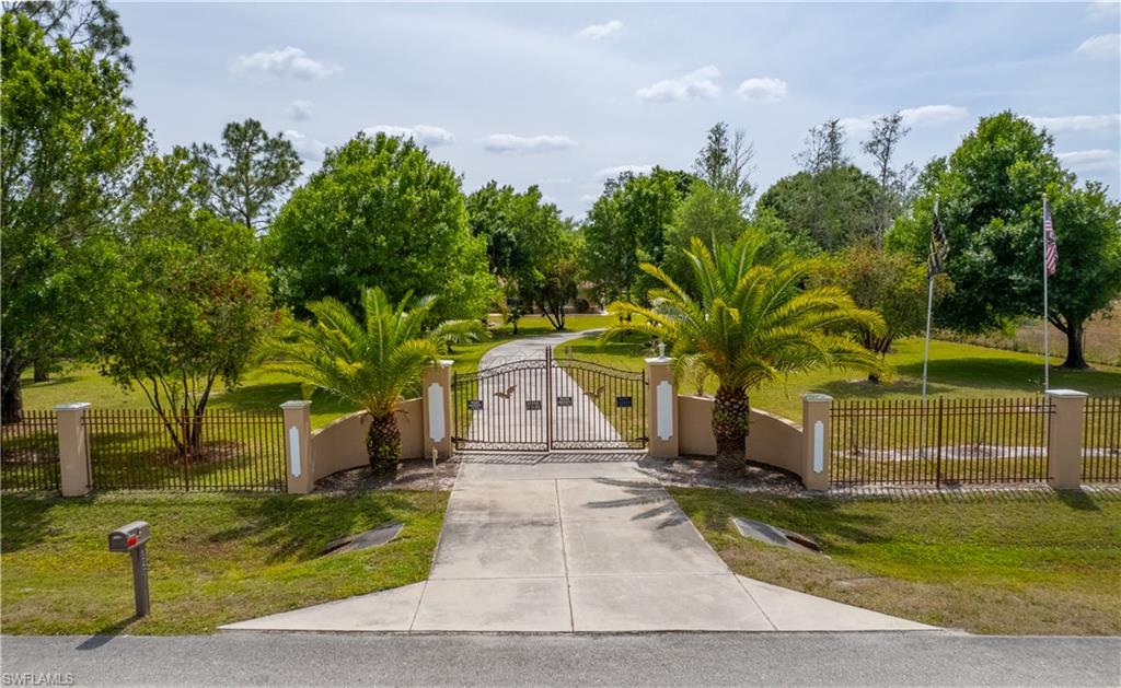 View of home's community with a gate, a fenced front yard, concrete driveway, and a yard