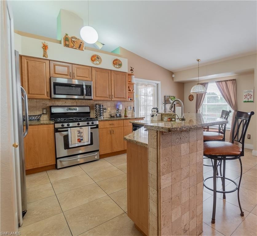 Kitchen featuring vaulted ceiling, a kitchen bar, appliances with stainless steel finishes, and light tile patterned floors