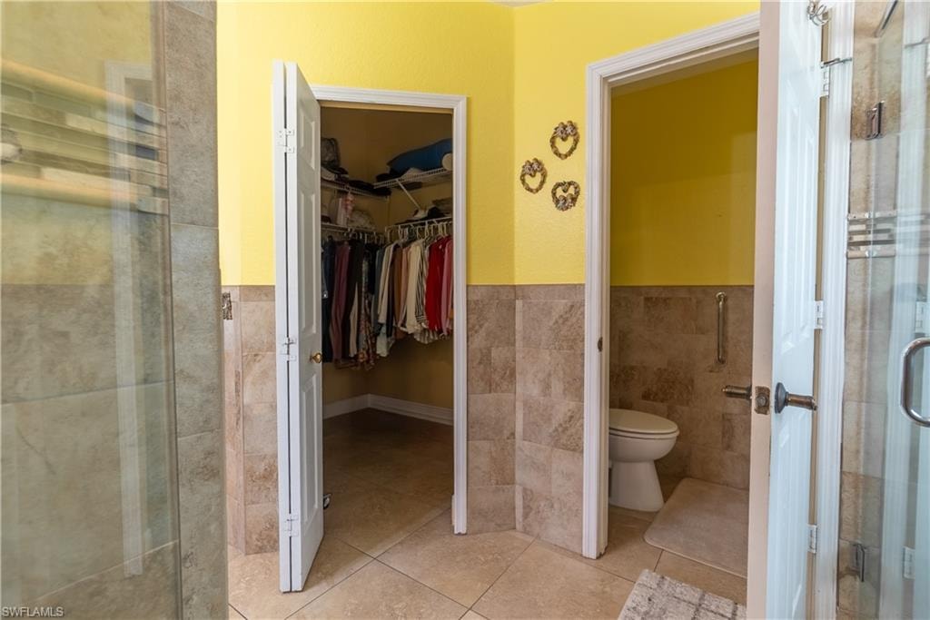 Full bath featuring tile walls, toilet, tile patterned floors, a stall shower, and a spacious closet