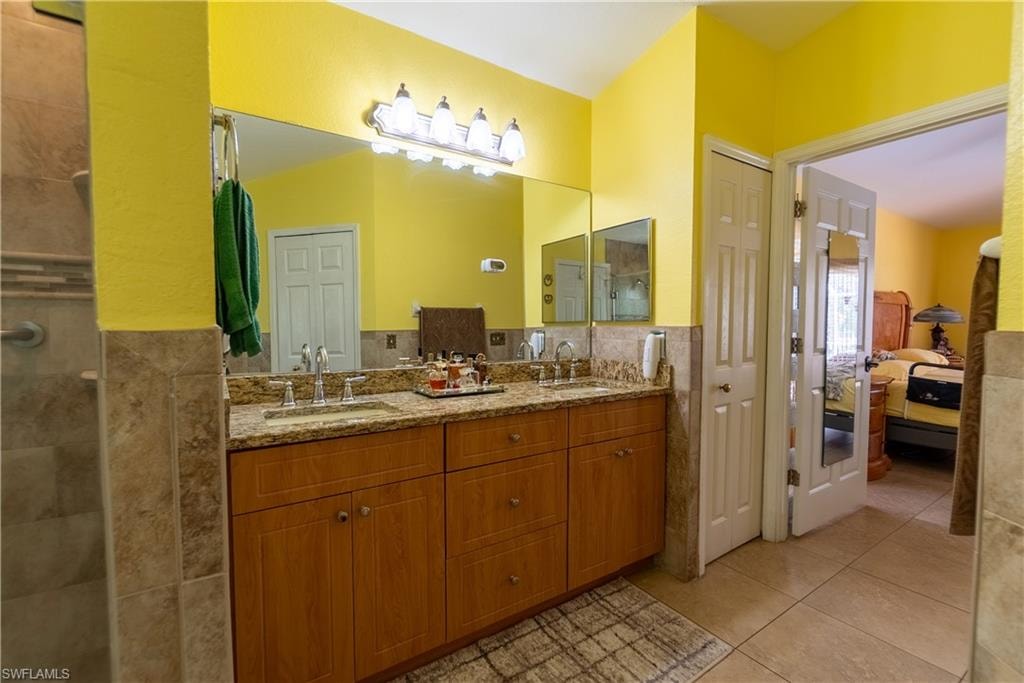 Ensuite bathroom with tile walls, a tile shower, a sink, and tile patterned floors