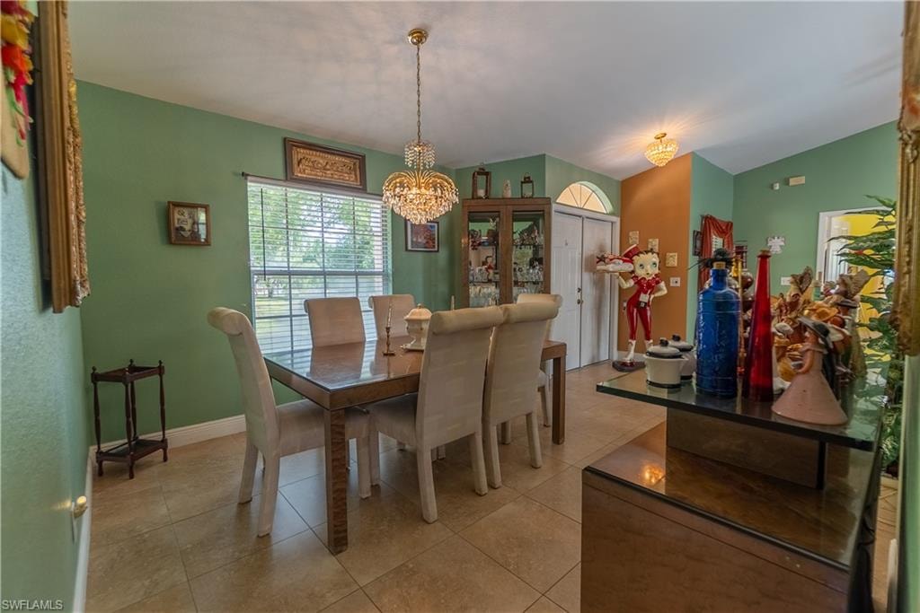 Dining area featuring light tile patterned flooring, lofted ceiling, baseboards, and a chandelier