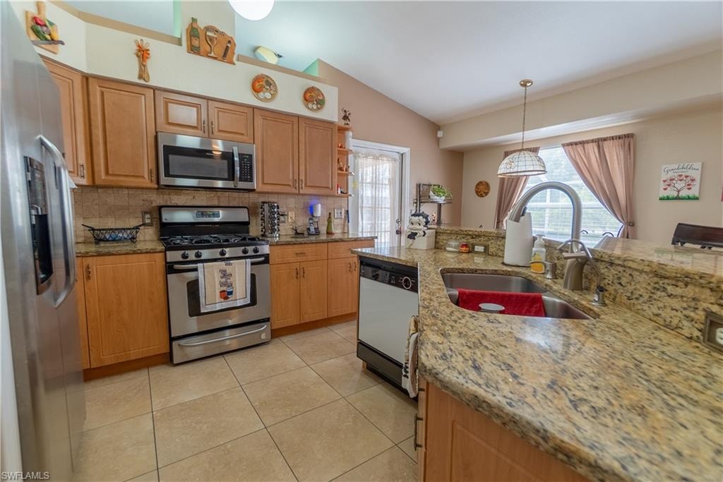 Kitchen with light tile patterned flooring, stainless steel appliances, lofted ceiling, a sink, and a wealth of natural light