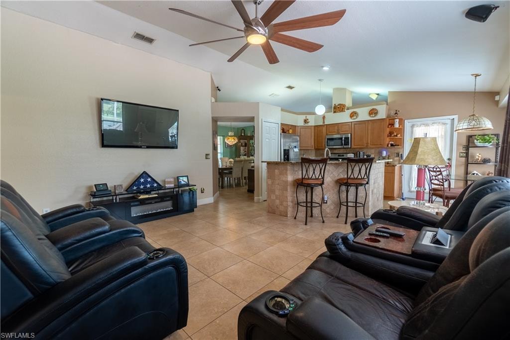 Living area with light tile patterned flooring, visible vents, lofted ceiling, and ceiling fan