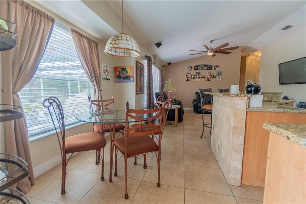 Dining room with vaulted ceiling, light tile patterned floors, baseboards, visible vents, and a ceiling fan
