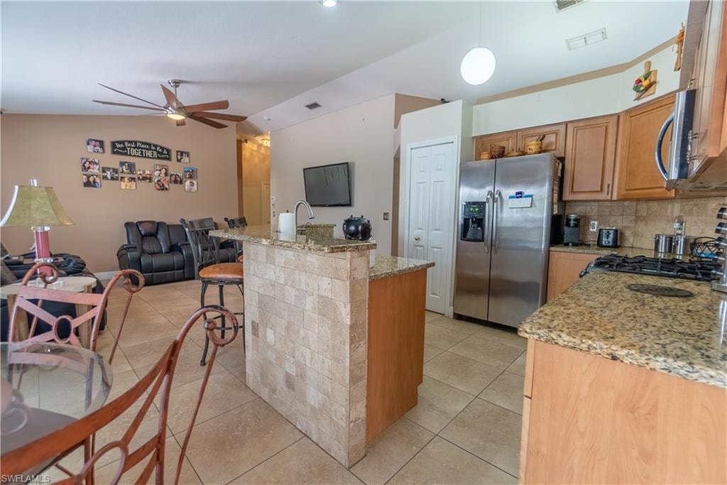 Kitchen with light tile patterned flooring, a ceiling fan, open floor plan, lofted ceiling, and stainless steel refrigerator with ice dispenser