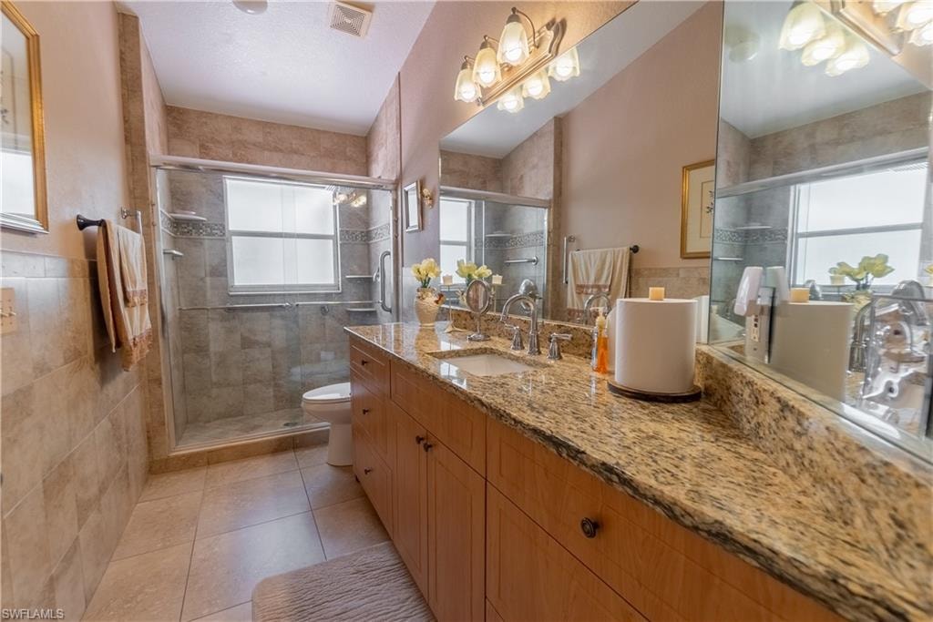 Bathroom featuring toilet, plenty of natural light, tile walls, and visible vents