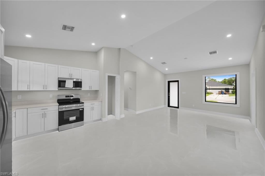 Open-concept living space with a contemporary kitchen featuring white cabinetry, light countertops, and stainless steel appliances