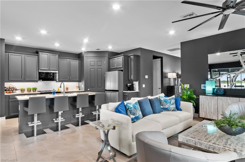 Open-concept living space featuring a kitchen island with seating, dark grey cabinetry, integrated stainless-steel appliances, and recessed lighting