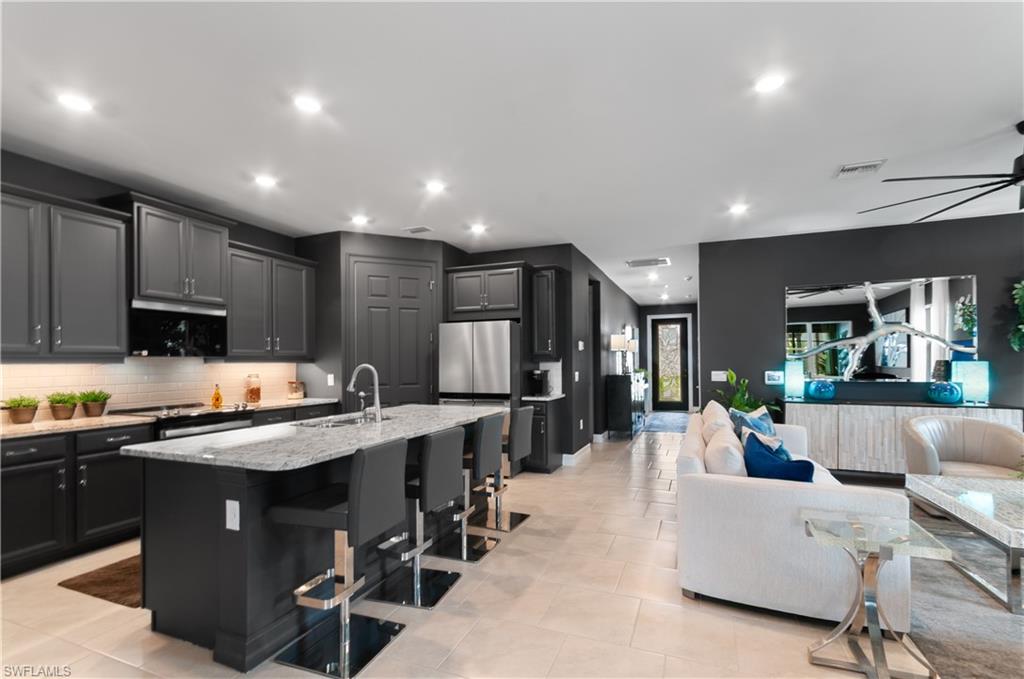 Open-concept living area featuring a kitchen with dark cabinetry, stainless steel appliances, a white tile backsplash, and a large island with seating