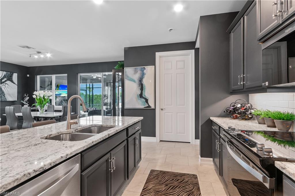 Kitchen featuring an expansive island with a double basin stainless steel sink, granite countertops, dark cabinetry, and tile flooring